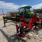 Red and black Palax MIDI wood splitter/processor attached to a trailer, with a green tractor in a lumber yard setting.